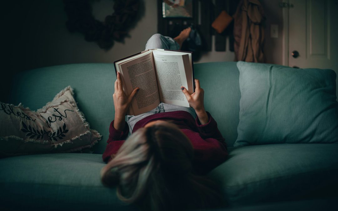 Woman reading a book sitting on a green sofa